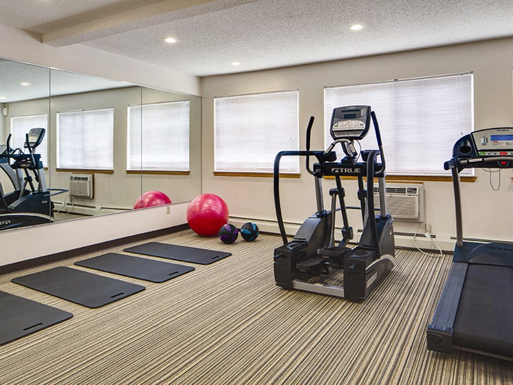 Fitness center with a treadmill, elliptical, yoga mats, and large mirrors
